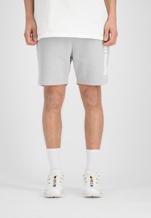 Shorts en coton gris avec poches latérales, texture lisse, et un logo "ALPHA" blanc sur le côté gauche. Portés avec des chaussettes blanches et des baskets.