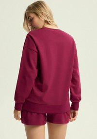 Bordowy sweatshirt o luźnym kroju, z żebrowanymi mankietami i dołem, w zestawieniu z koordynującymi szortami w tym samym kolorze i fakturze materiału.