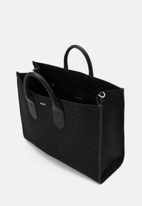 Czarna torba typu tote z gładkimi skórzanymi uchwytami, z monogramem na tkaninowym wierzchu, otwarta od góry, z kieszenią wewnętrzną i srebrnym detalem z logo.