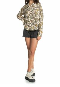 Blommönstrad skjorta med knappar i krämfärg, kombinerad med svarta denimshorts och ljusa stövlar med svarta sulor; avslappnad passform och korta ärmar.