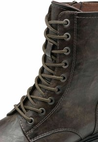 Brown leather ankle boot with metal eyelets, round laces, and a smooth finish. Features a reinforced toe and contrasting stitching detail.