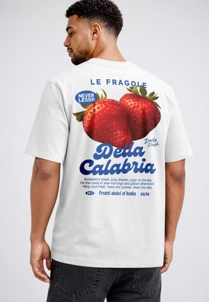 Man wearing white T-shirt with large printed strawberries and Italian text on the back, facing sideways against a plain background.