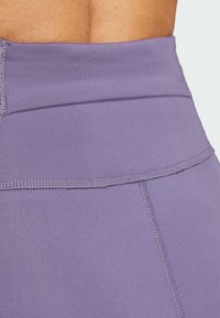 Leggings taille haute en tissu lavande avec une texture lisse, présentant des coutures flatlock et une large ceinture pour le confort.