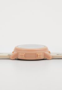 Vue latérale d'une montre-bracelet beige avec deux boutons carrés et un bracelet à motif floral posé à plat sur une surface blanche.