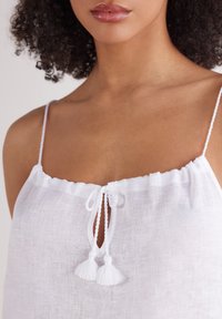 Witte linnen top met dunne schouderbandjes, een ronde halslijn en een voorste knoopdetail met twee franjes. Lichtgewicht en met een gestructureerde stof.