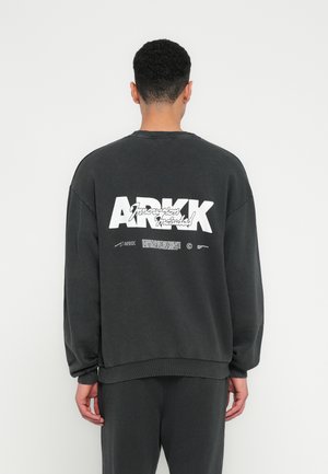 Dark gray sweatshirt with long sleeves, ribbed cuffs, and hem. Features white printed text and branding on the back. Cotton material.