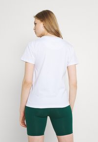 Hvit bomull t-skjorte med korte ermer, rund hals og tettsittende fasong, brukt sammen med mørkegrønne trening-shorts. Enkel og upryddig design.