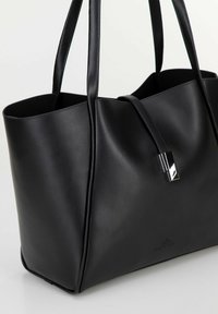 Borsa tote in pelle nera con texture liscia, hardware argentato lucido, design minimalista e branding ben visibile alla base.