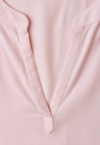 Tissu rose clair avec un décolleté en V comportant une patte étroite cousue et une couture décorative subtile le long des bords.