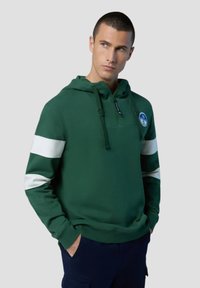 Felpa verde con strisce bianche sulle spalle, colletto con zip a metà, cordino regolabile e patch con logo. Realizzata in morbido tessuto testurizzato.