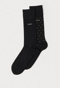 Schwarze Socken mit glatter Textur; eine einfarbig schwarz, die andere schwarz mit gelben Punkten. Beide haben ein kleines "BOSS"-Logo nahe dem oberen Rand.