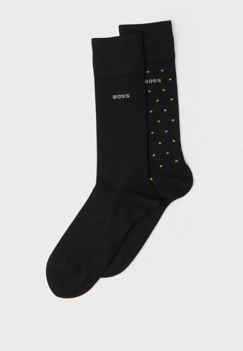 Schwarze Socken mit glatter Textur; eine einfarbig schwarz, die andere schwarz mit gelben Punkten. Beide haben ein kleines "BOSS"-Logo nahe dem oberen Rand.