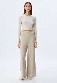Pitkähiha, cropped-top vaaleanbeige ribbikankaasta, yhdistettynä leveisiin vaaleanbeigeihin housuihin. Molemmilla on pehmeä rakenne ja minimaalinen muotoilu.