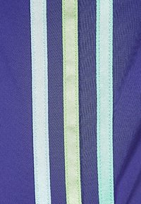 Lila tyg med tre vertikala ränder i olika nyanser av blått och grönt. Texturen är jämn, med kontrasterande satinstygn.