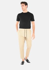 Maglietta nera a righe con maniche corte, pantaloni beige con cintura elastica e cordino, e scarpe nere slip-on con suole bianche.