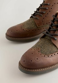 Brown leather shoes with a textured toe, herringbone fabric detailing on the sides, and dark laces, featuring brogue-style perforations.