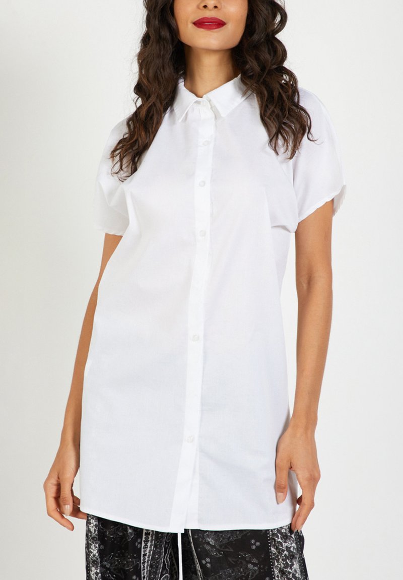 Camisa blanca de botones con mangas cortas, con un cuello clásico y un ajuste ligeramente holgado. Fabricada en un tejido ligero, de textura suave.