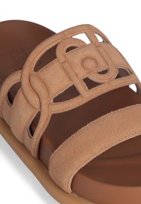 Tan suede slide sandal with a wide strap featuring cut-out geometric design, soft brown insole, and beige rubber outsole.