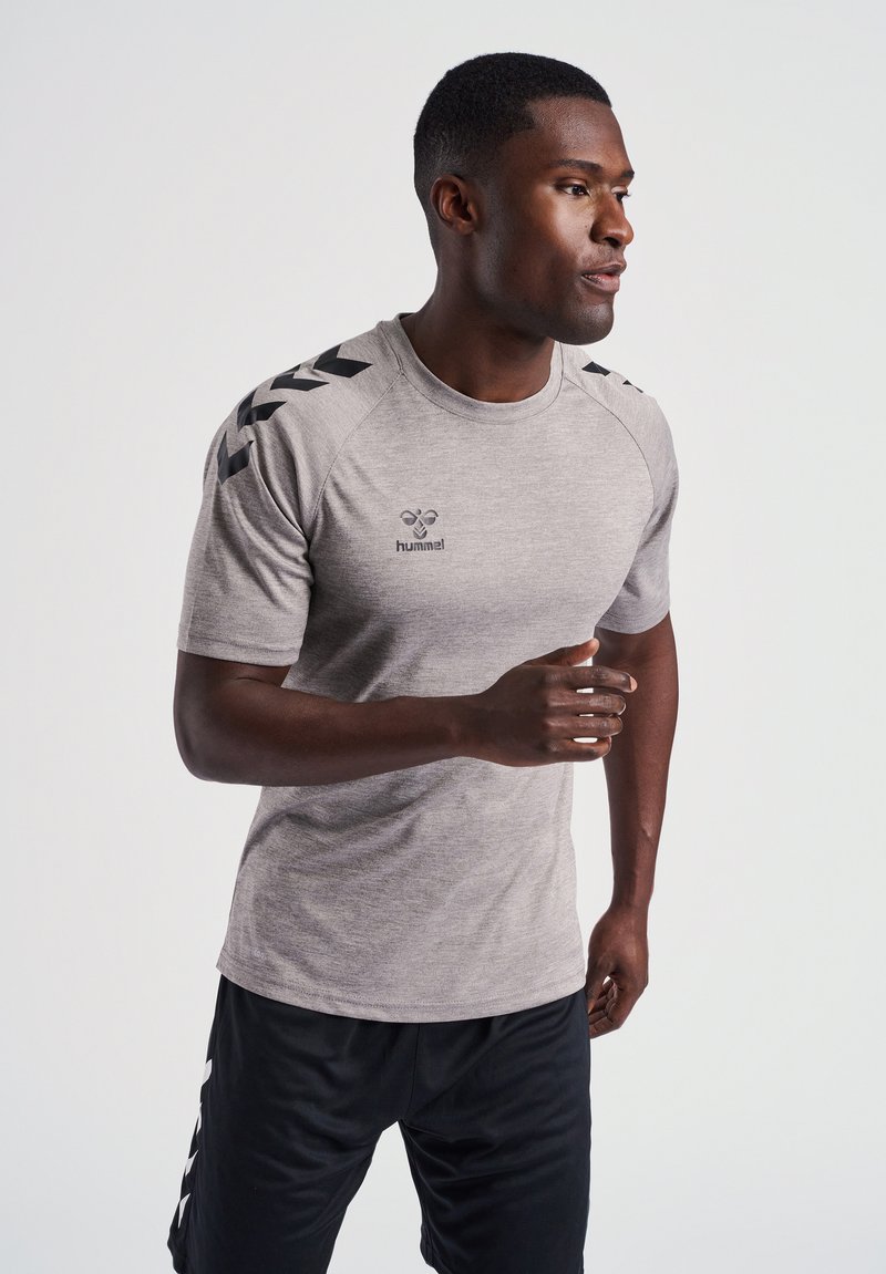 T-shirt de sport gris à manches courtes avec des accents noirs et un logo sur la poitrine, associé à un short noir avec des rayures blanches sur les côtés.