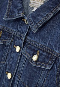 Jeansjacka i mörkblå färg med metalldekorationer och kontrasterande sömmar. Inkluderar bröstfickor och en klassisk kragdesign.