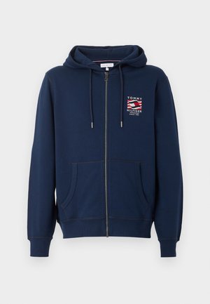 Sweat à capuche bleu marine zippé intégralement avec poches avant, capuche à cordon et petit patch logo Tommy Hilfiger sur le côté gauche de la poitrine.
