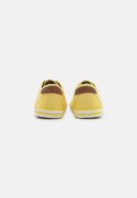 Yellow canvas shoes with a brown leather heel accent and white rubber soles, featuring yellow and white striped detailing.