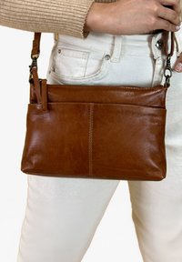 Ruda odinė crossbody rankinė su lygiu paviršiumi, stačiakampio formos ir priekinėmis kišenėmis, turinti nuimama pečių juostą.