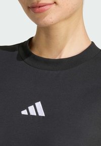 Czarny bawełniany T-shirt z okrągłym dekoltem, z małym białym haftowanym logo Adidas na klatce piersiowej. Gładka tekstura, casualowy design.