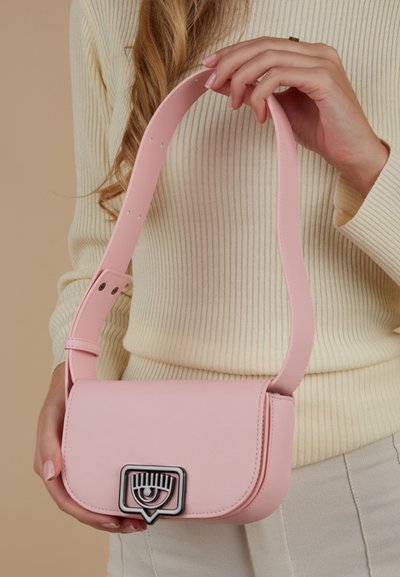 Sac bandoulière en cuir synthétique rose avec un rabat plat, une sangle réglable et une quincaillerie en métal avec un logo œil. Texture lisse avec un minimum de détails.