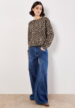 Haut à manches longues en imprimé léopard beige et marron, associé à un jean large taille haute bleu. Texture lisse avec coupe décontractée.