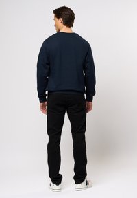 Mørkeblå genser med rund hals, med lange ermer. Kombinert med slim-fit svarte bukser og hvite sneakers med fargede detaljer.