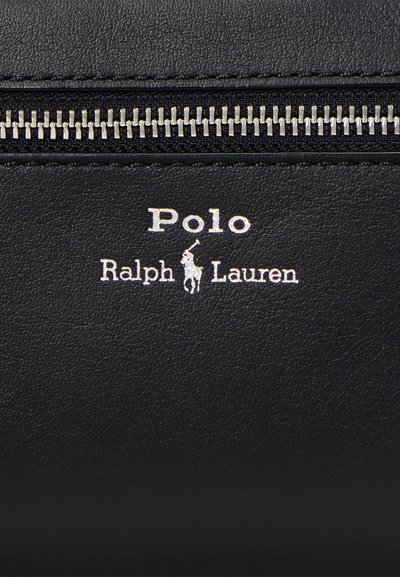 Crna kožna površina sa srebrnim patentnim zatvaračem i bijelim Polo Ralph Lauren logom s prikazom igrača polo na konju ispod patentnog zatvarača.