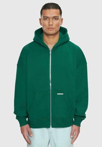 Grøn zip-up hættetrøje med en stor hætte, frontlommer og ribbede manchetter. Glat bomuldsstof med en afslappet pasform.