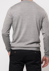 Grå tröja med rund hals och långa ärmar, med en slät yta och ribbat nederkant, bärs över mörka byxor.