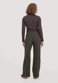 Lässige, dunkelgrüne Hose mit weicher Textur und weitem Bein, kombiniert mit einem eng anliegenden, langärmeligen, dunkelvioletten Oberteil.