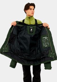 Zielona kurtka puchowa z gładkim, błyszczącym wykończeniem. Wnętrze zawiera czarne podszewki, szczegóły metki oraz strukturalne kieszenie. Zamek błyskawiczny z zatrzaskami.