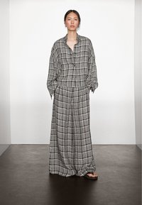 Gråt og hvidt ternet todelt sæt lavet af letvægtsstof; består af en løs skjorte med knapper og vidde bukser.