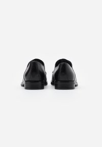 Scarpe in pelle nera con una finitura liscia, bordi curvi, tacchi a blocco bassi e lati aperti per una migliore traspirabilità. Design minimalista, senza accessori visibili.