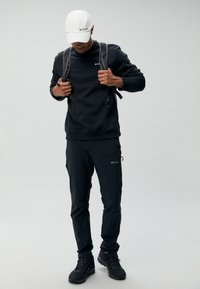 Sweatshirt et pantalon noirs avec le logo Columbia. Casquette blanche. Sac à dos gris. Chaussures noires robustes. Tissu lisse avec un design fonctionnel et des zippers.