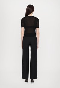 Czarny, prążkowany top z krótkim rękawem o dopasowanym kroju, zestawiony z szerokimi czarnymi spodniami. Model widziany od tyłu, styl minimalistyczny.