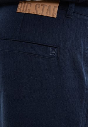 Marineblaue Hose aus strukturiertem Stoff, mit einem dezenten Logo auf der Gesäßtasche und einem tanfarbenen Lederschild mit geprägter Aufschrift "BIG STAR".