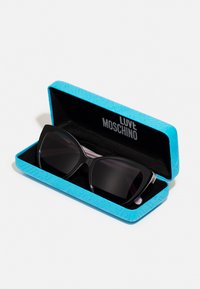 Black cat-eye sunglasses in a light blue hard case with embossed patterns, featuring a soft black interior and bold brand logo inside.