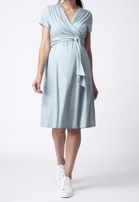 Ljusblå omlotklänning med korta ärmar, vita prickar och en knytning i midjan. Matchad med vita sneakers. Slät tygtextur.