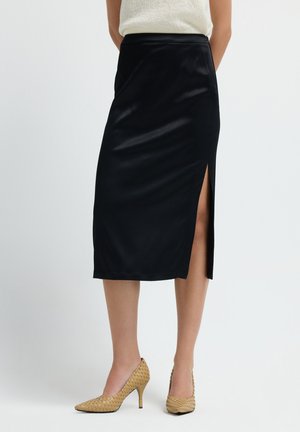 Schwarzer Satin-Bleistiftrock mit einem seitlichen Schlitz. Glatte Textur, knielang, hohe Taille. Kombiniert mit gewebten beigefarbenen High Heels.