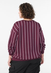 Bordo kapuća sa belim vertikalnim prugama, opuštenog kroja, rebrastim manžetama i izrezom. Mekana tkanina sa blago strukturiranom površinom.