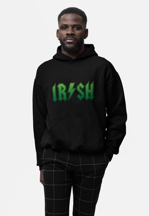 Schwarzer Hoodie mit grünem grafischem Text "IRISH" und Blitzelementen. Kombiniert mit schwarz-karierter Hose, was einen lässigen Look unterstreicht.
