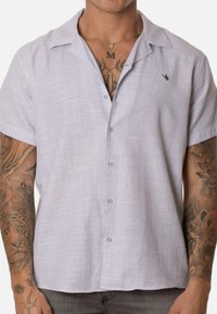 Camisa de lino de manga corta, color gris claro, con un patrón texturizado, cuello con muesca y cinco botones en el frente. Logo bordado en el pecho.