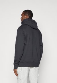 Tamsiai pilkas megztinis su gausia kapišonu, raukšlėmis apykakle ir apačia, pasižymintis tekstūruotu audiniu ir laisvu kirpimu, derinamas su pilkais kargo sportiniais džinsais.