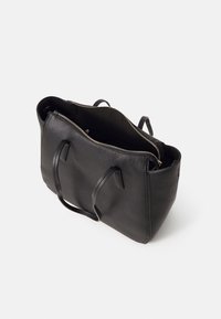 Sac cabas en cuir noir texturé avec doubles poignées et fermeture éclair supérieure partiellement ouverte laissant apparaître la doublure intérieure.