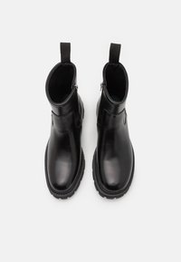 Botas de tobillo de cuero negro con un acabado liso, cremalleras laterales, tiradores y suelas de goma que presentan un patrón de tracción robusto.